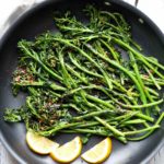 Sauteed broccolini is served with lemon slices.