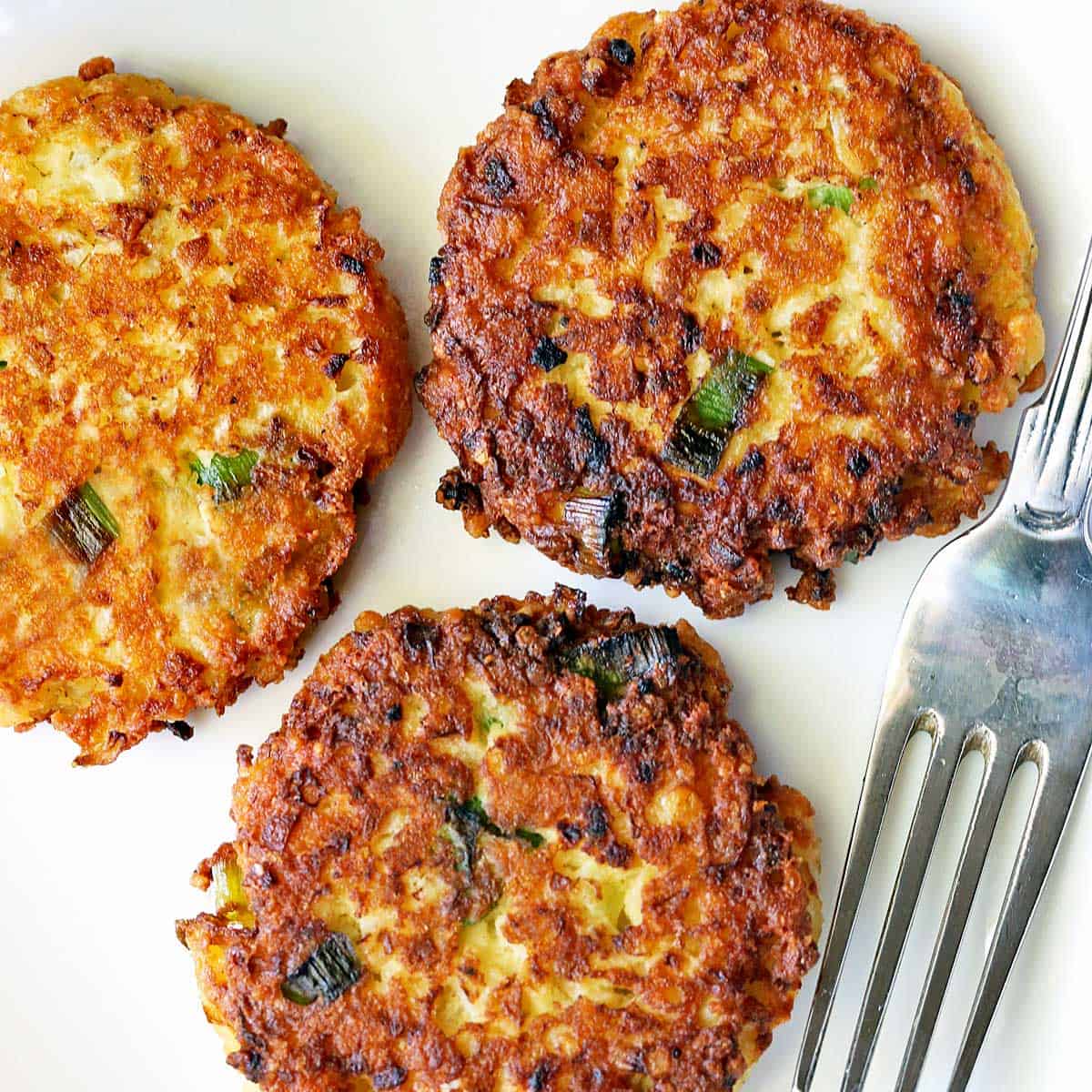 Cauliflower fritters are served on a white plate with a fork.