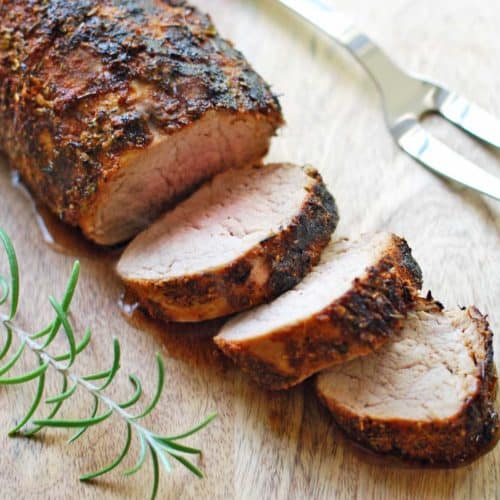 Roasted pork tenderloin is sliced and served on a wooden cutting board.