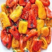 Roasted mini peppers are served on a white plate.