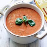 Cold tomato soup is garnished with a basil leaf.