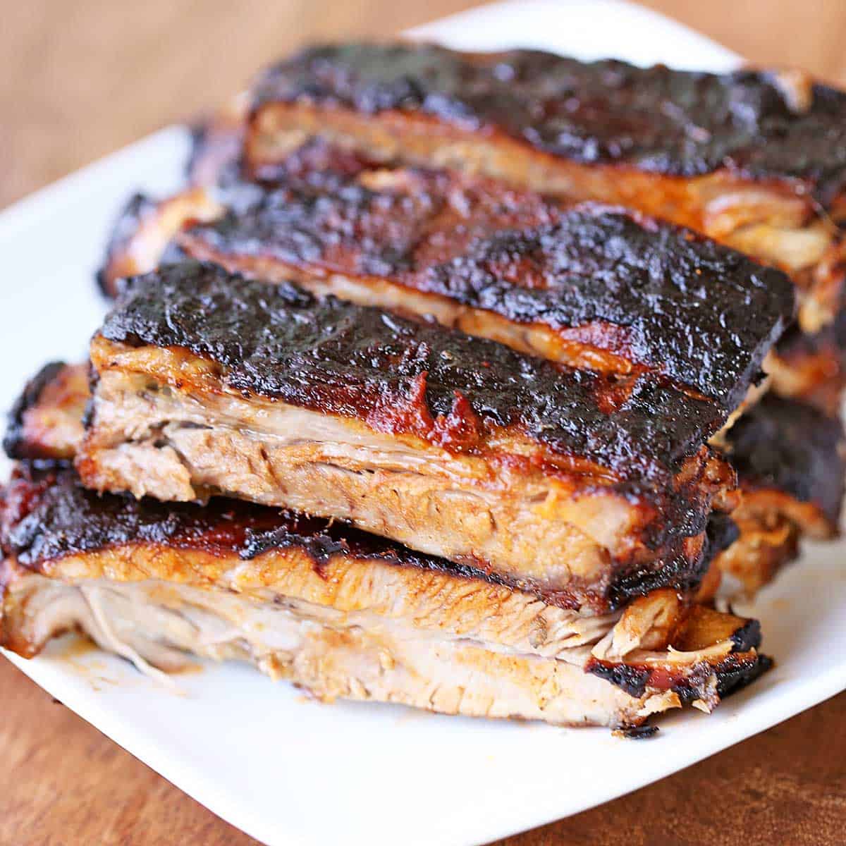 Oven-baked ribs are stacked on a white plate.