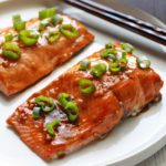 Asian salmon is served on a white plate with chopsticks.