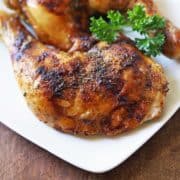 Chicken leg quarters are served on a white plate, garnished with parsley.