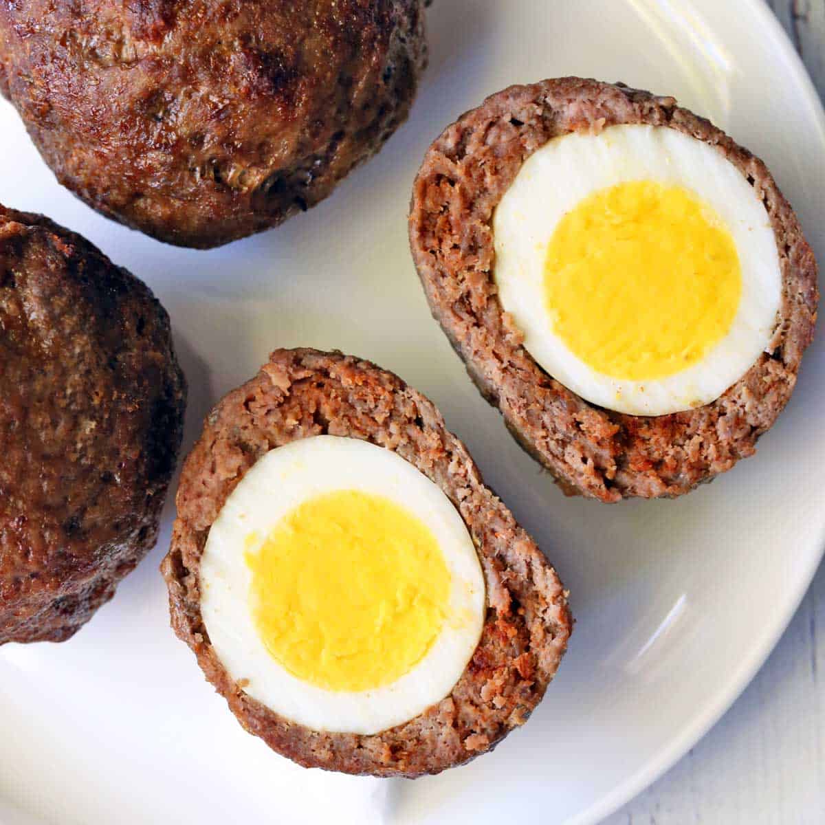 Baked Scotch eggs are served on a white plate.