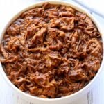 Slow cooker pulled pork is served in a white bowl.