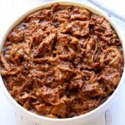 Slow cooker pulled pork is served in a white bowl.