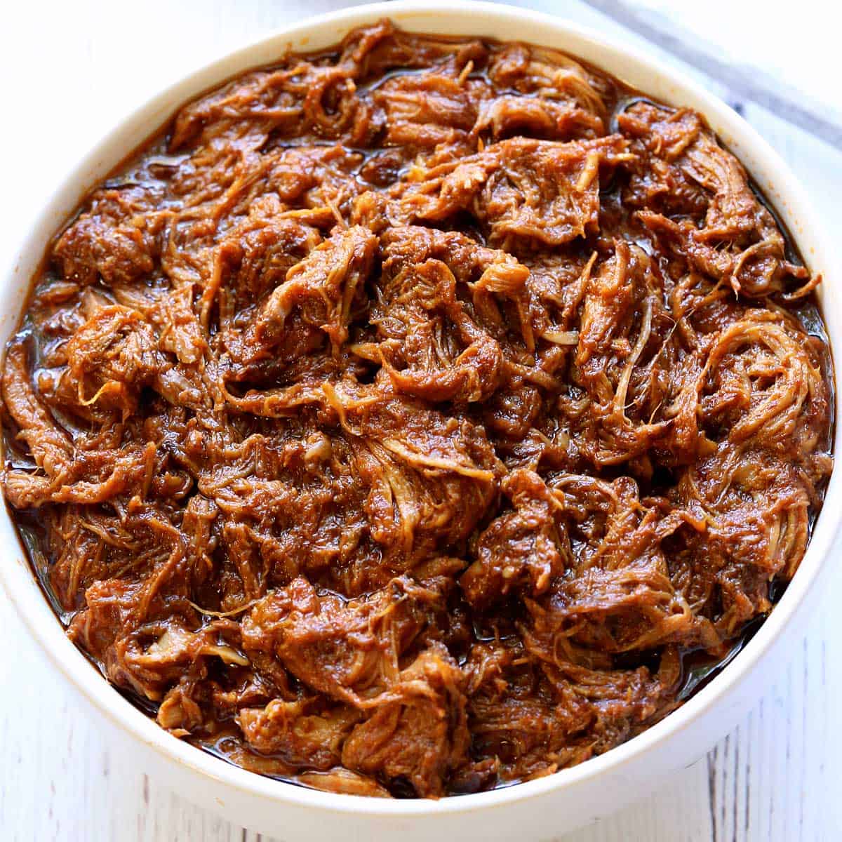 Slow cooker pulled pork is served in a white bowl.