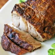 Pork roast is served on a white platter with broccoli.
