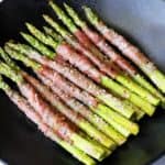 Prosciutto wrapped asparagus is served on a dark plate.