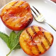 Grilled peaches are served on a white plate with a fork.