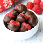 Chocolate covered raspberries are served in a white bowl.
