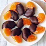 Chocolate covered oranges are served on a white plate.