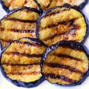 Grilled eggplant slices are served on a white plate.