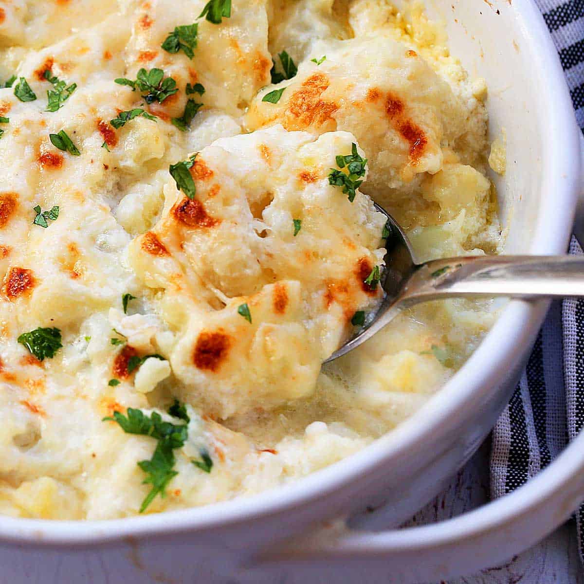 Cauliflower gratin is served in a white baking dish with a spoon.