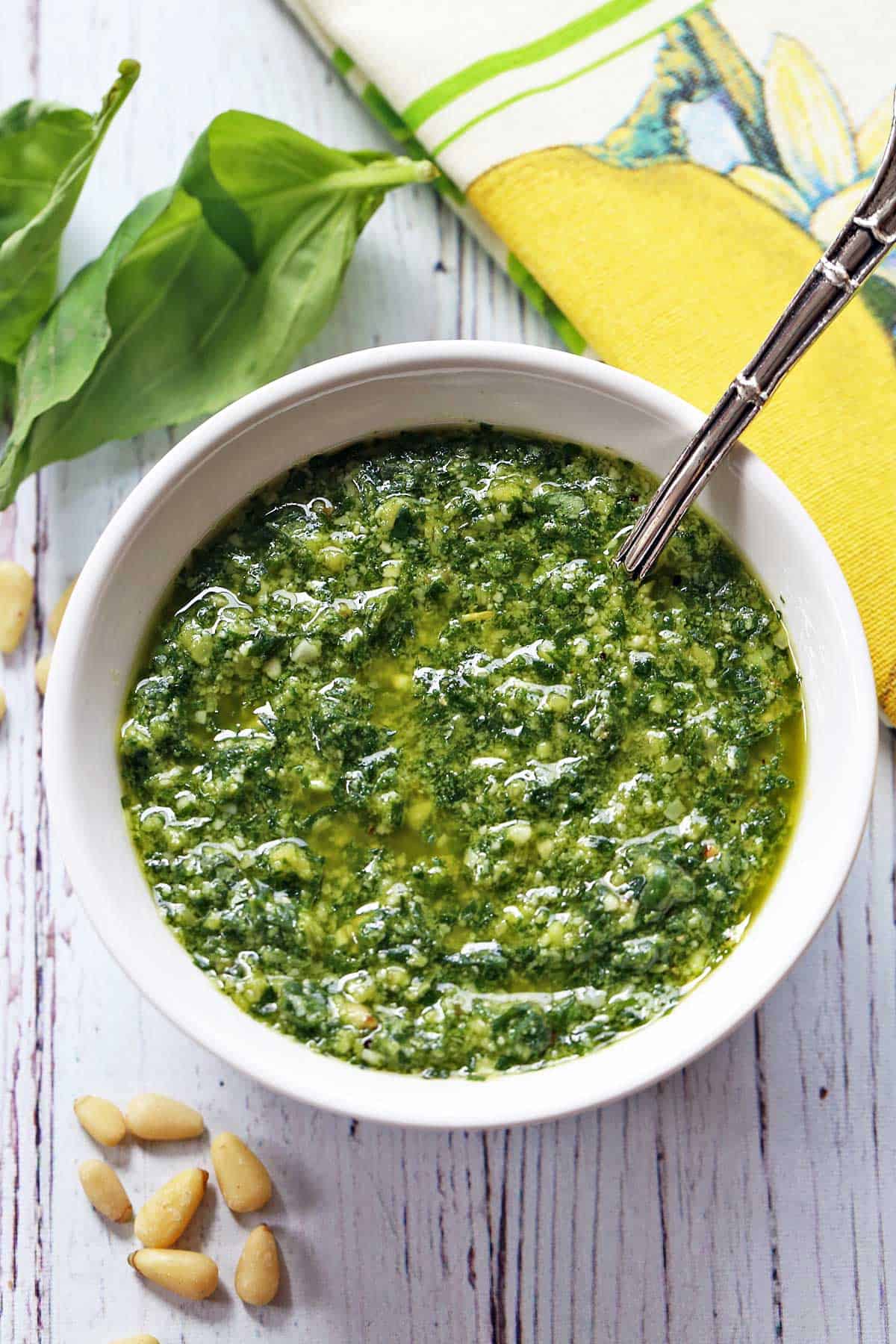 Homemade pesto sauce is served in a white bowl with a spoon. 