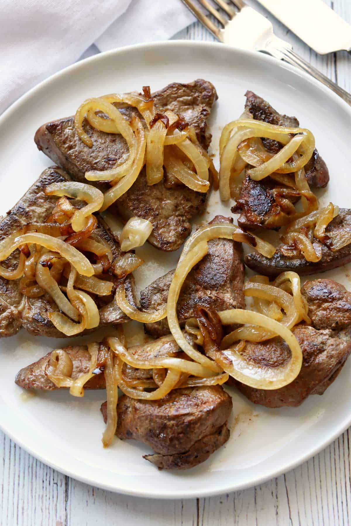 Liver and onions are served on a white plate.