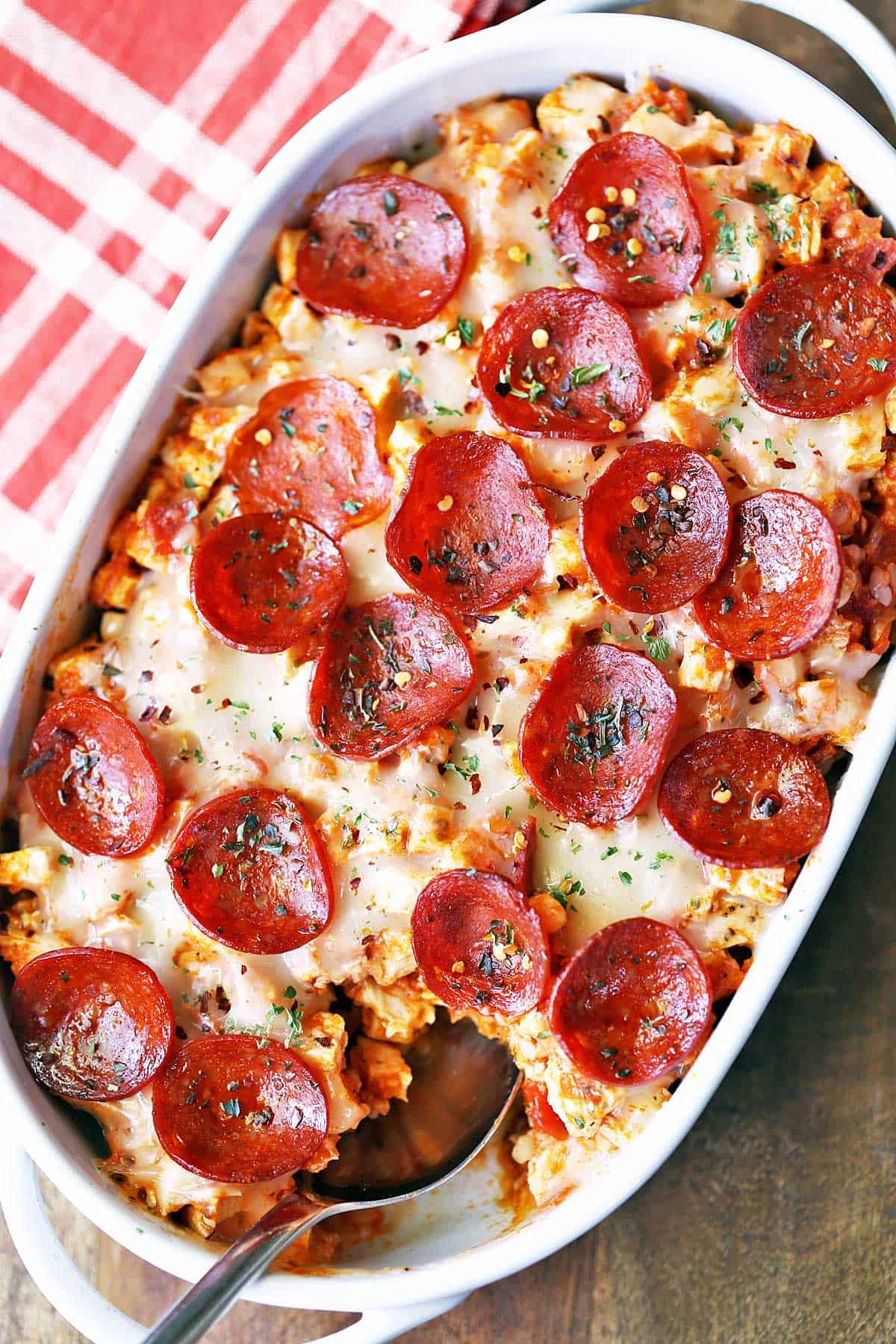 Keto pizza casserole is served in a white baking dish with a serving spoon. 