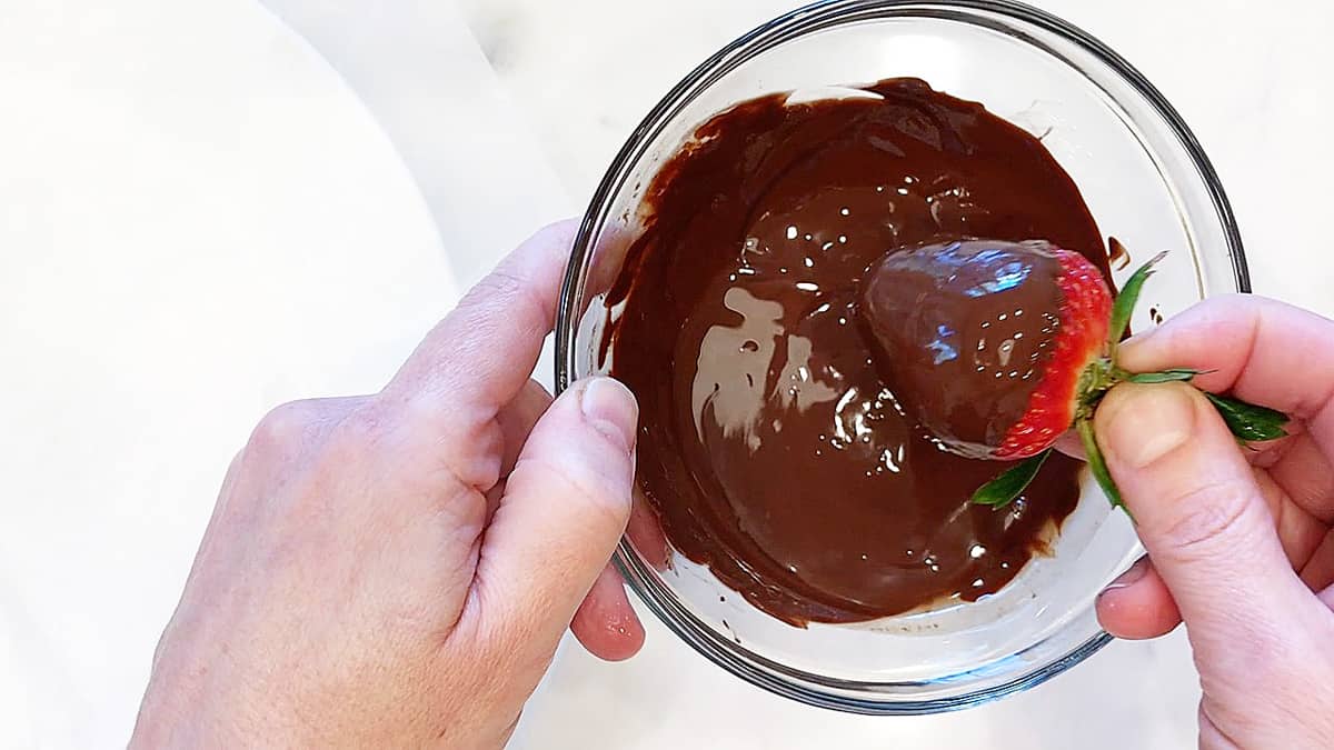 Dipping a strawberry into melted chocolate.