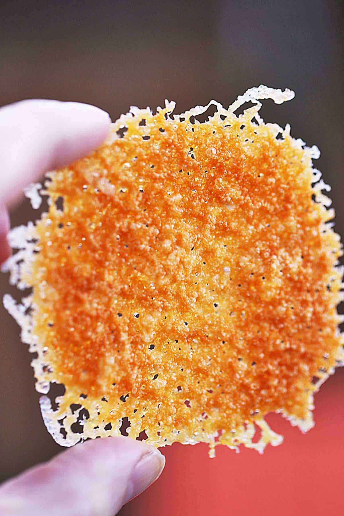 A hand is holding up a keto cheese cracker.