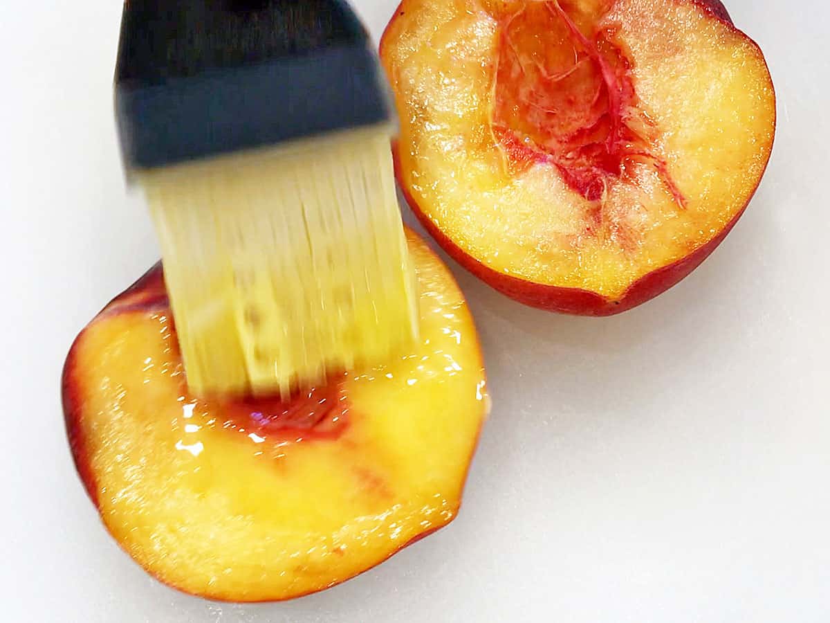 A peach cut in half is brushed with melted butter.