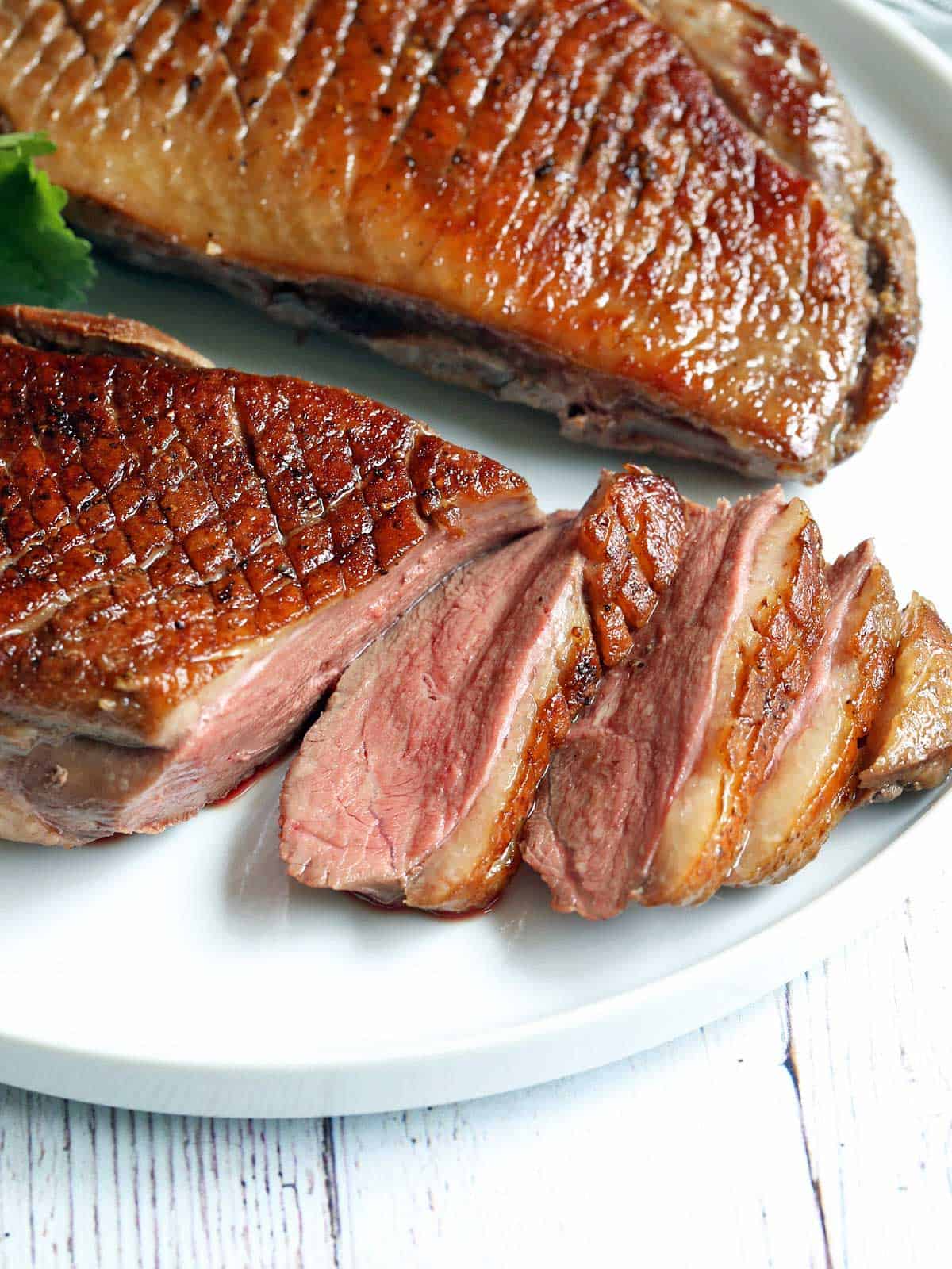 Cooked duck breast is served on a white plate. 
