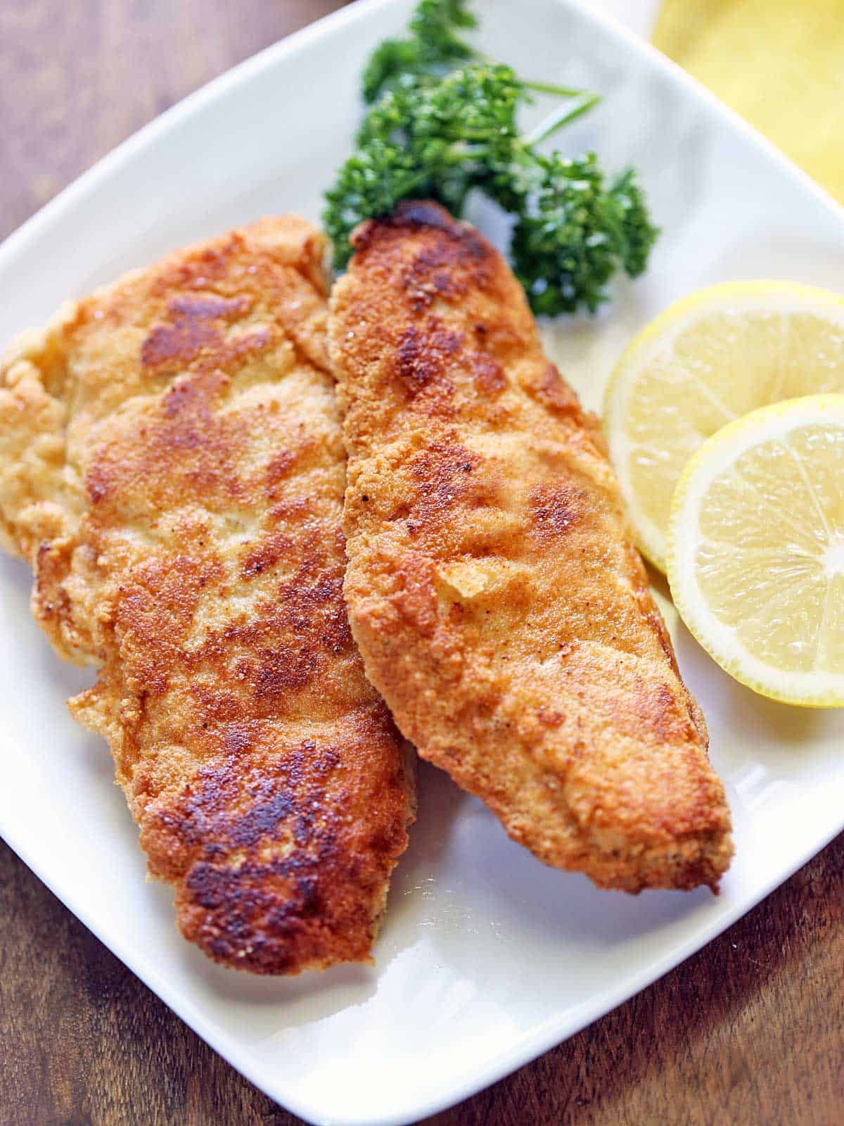 Two pieces of keto fried fish served with lemon slices.