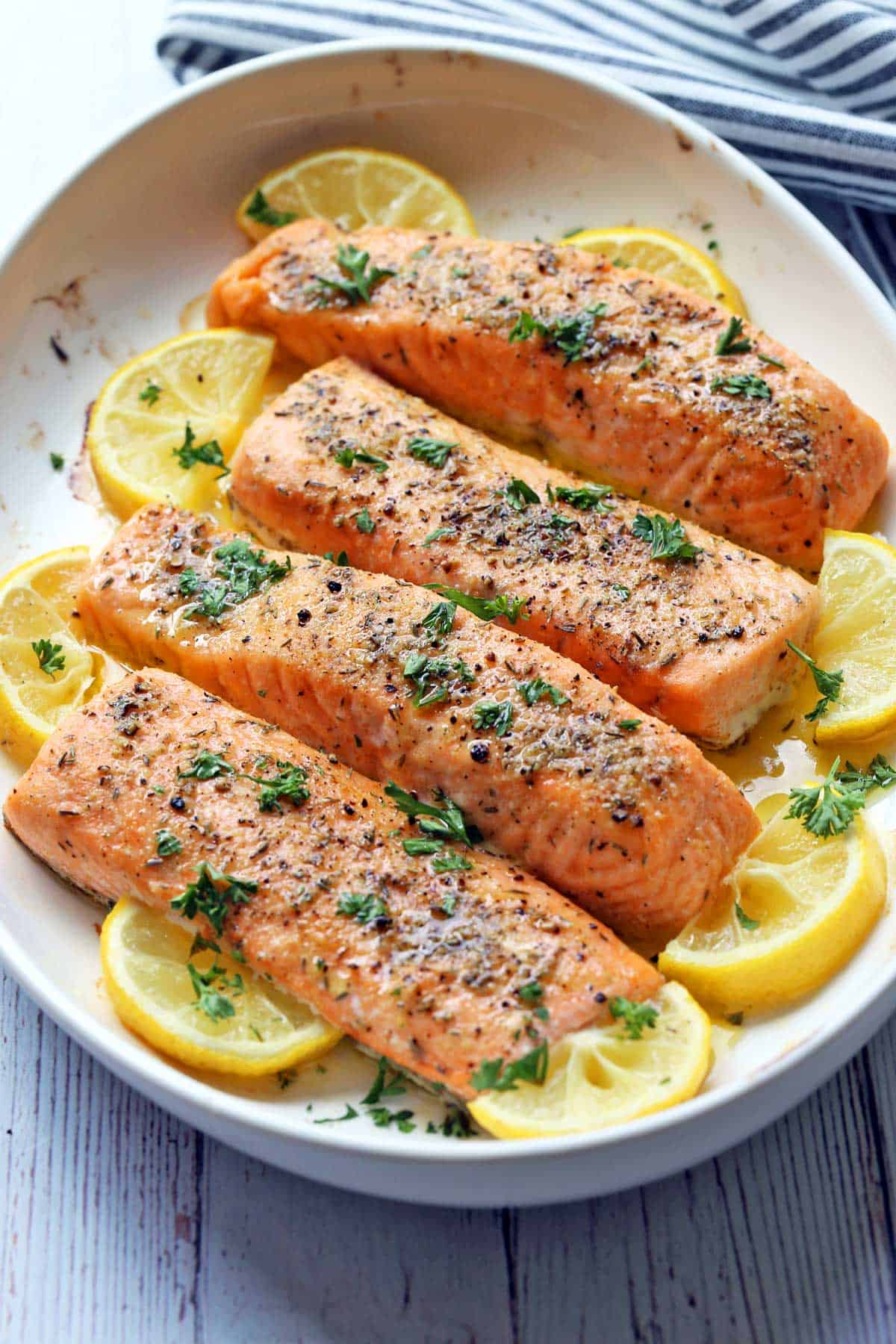 Four fillets of baked salmon are served in a white dish. 