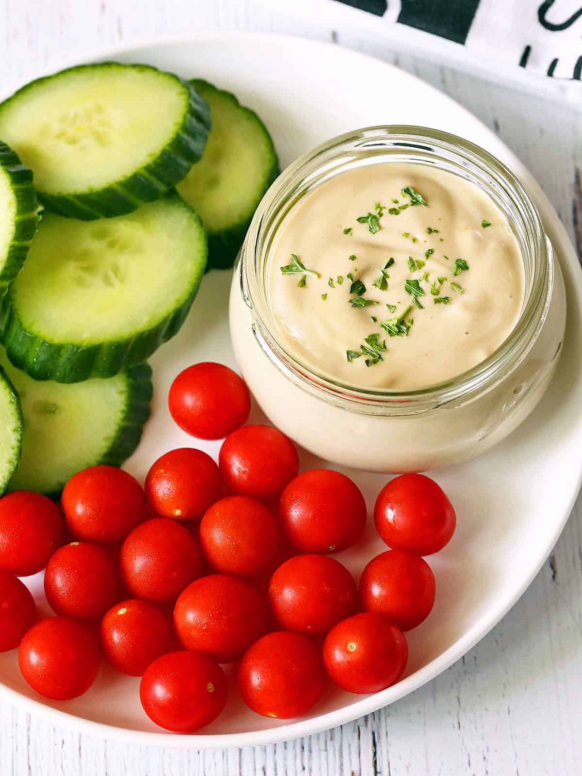 Tahini sauce is served with cucumber slices and tomatoes. 
