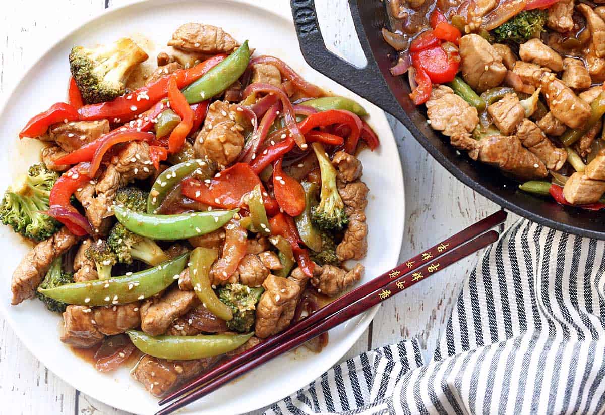 Pork stir-fry served on a white plate with chopsticks.