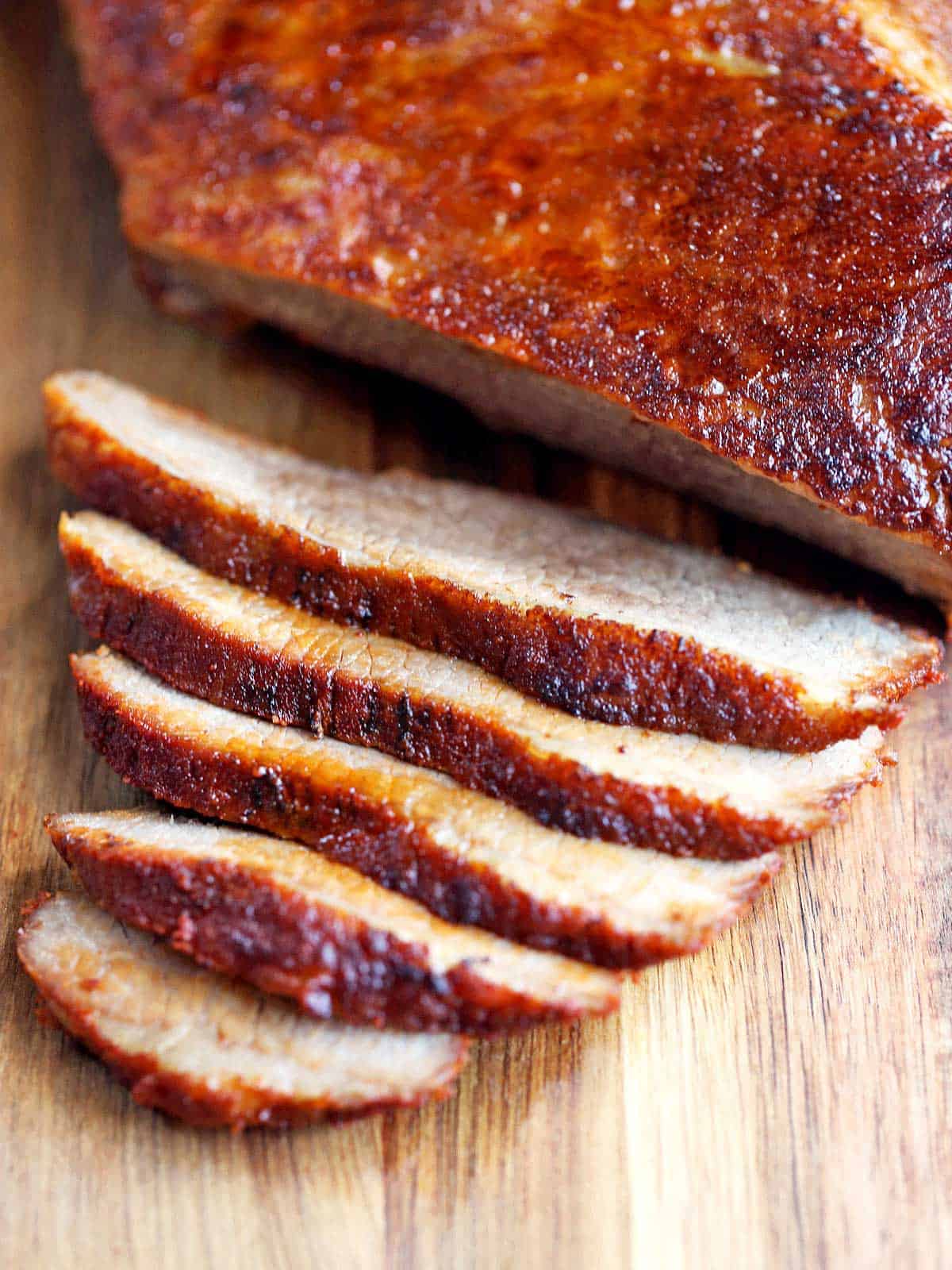 Sliced beef brisket is served on a wooden cutting board.