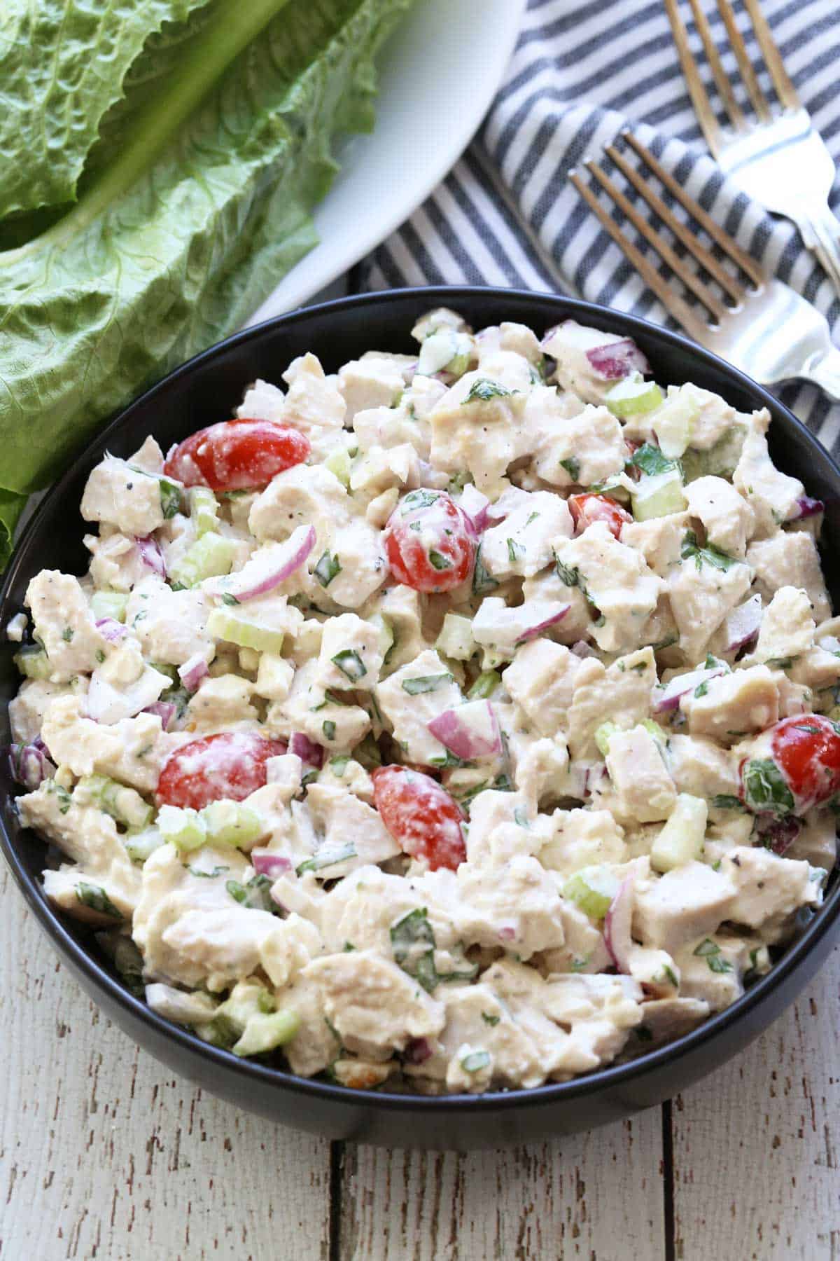 Chicken salad is served in a black bowl with a napkin and forks. 