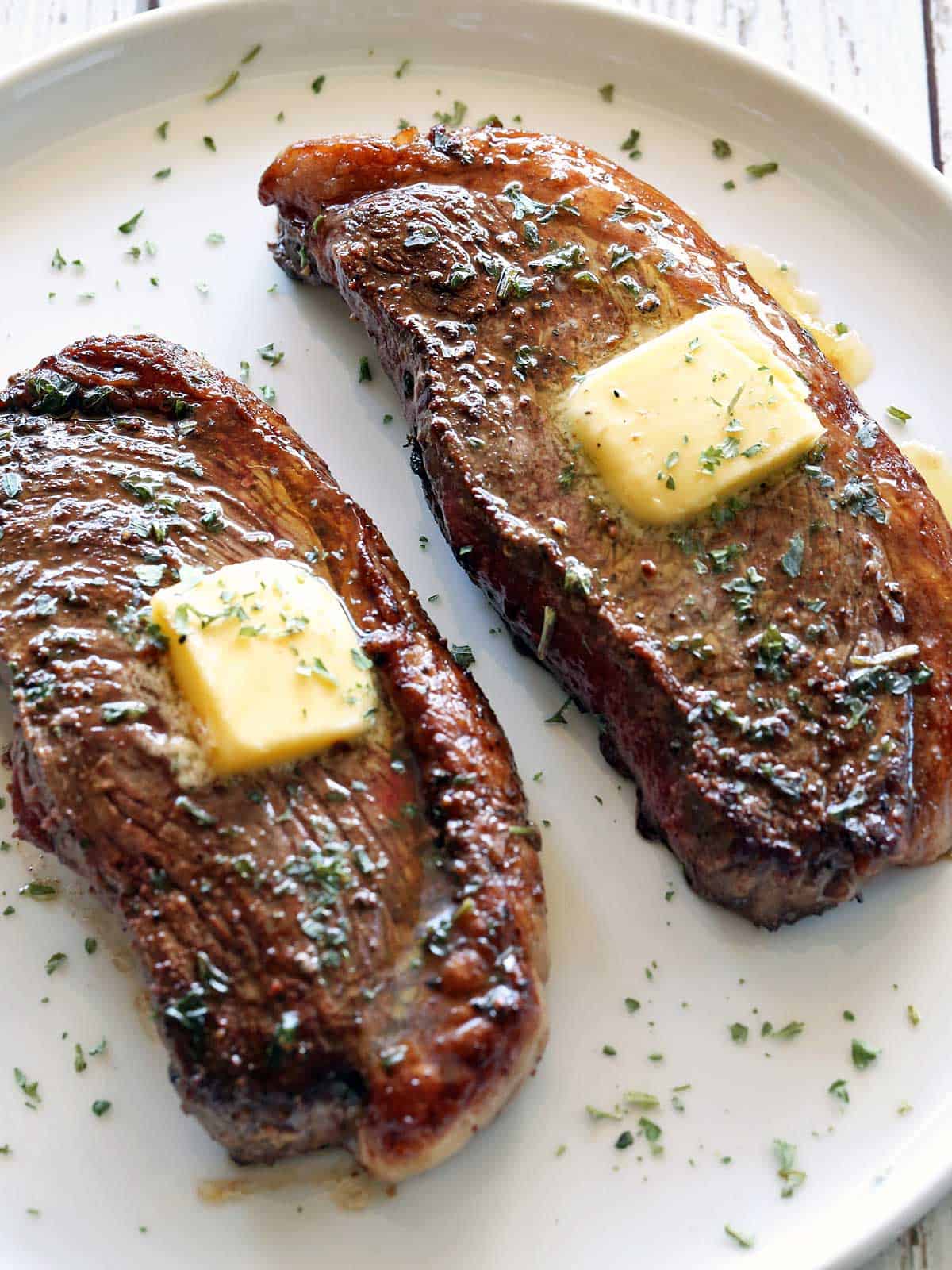 Two picanha steaks are served on a white plate and topped with butter.