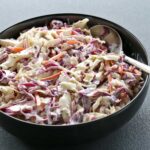 Homemade coleslaw is served in a black bowl.