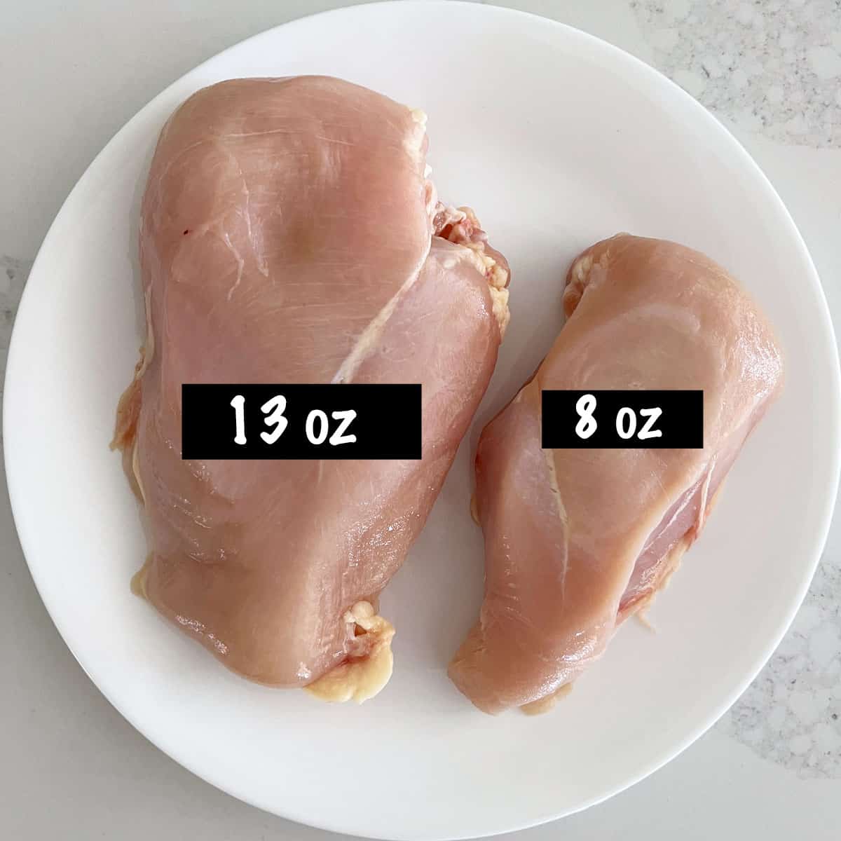 A large chicken breast next to a small one on a white plate.