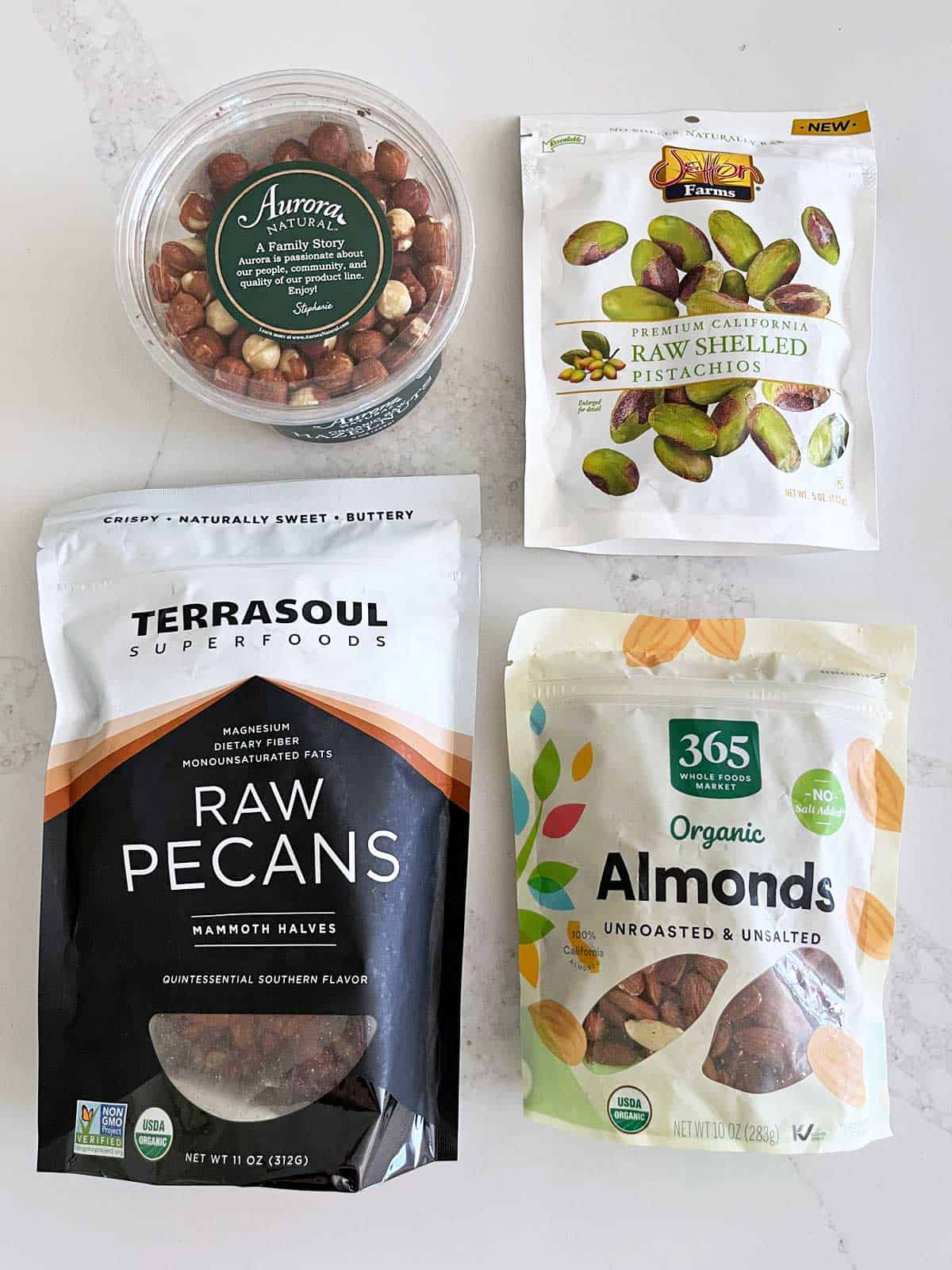 Four bags of packaged raw nuts: hazelnuts, pistachios, pecans, and almonds.