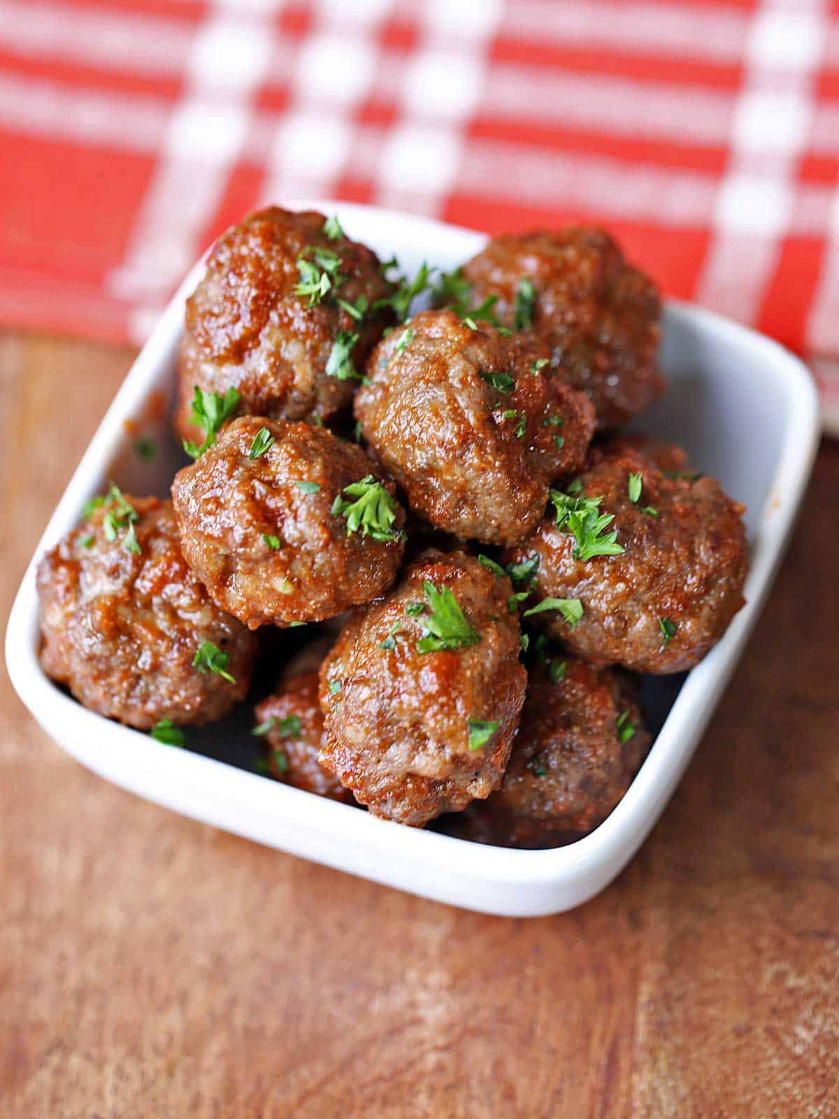 Baked meatballs without breadcrumbs are served in a white bowl and garnished with chopped parsley.
