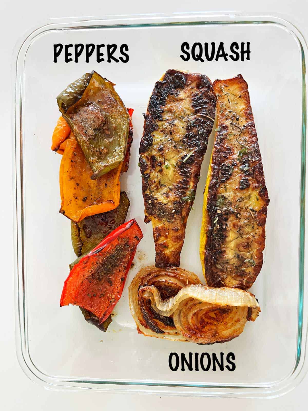 A food storage container with roasted squash, peppers, and onions.