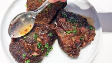 Spooning pan juices on top of slow cooked beef cheeks.