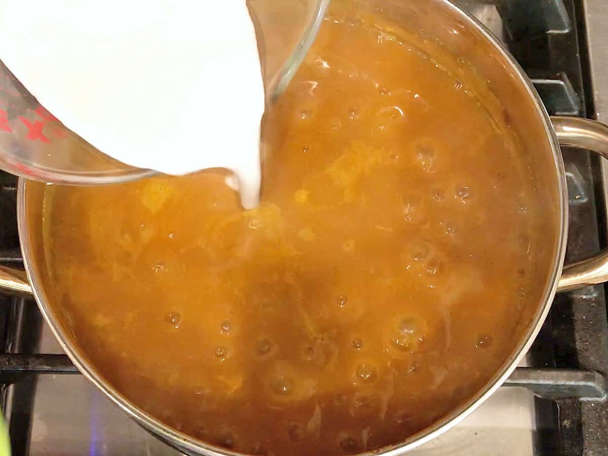 Adding coconut milk to pumpkin curry soup in the saucepan.