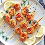 Grilled scallops are served with lemon slices.