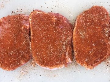 Seasoned pork chops on a cutting board.