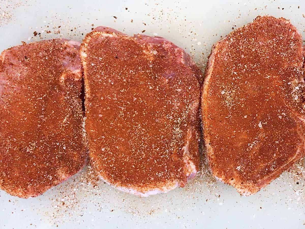 Raw pork chops are coated with spices.