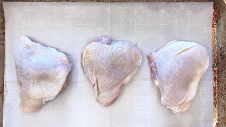Raw chicken thighs arranged on a baking sheet.