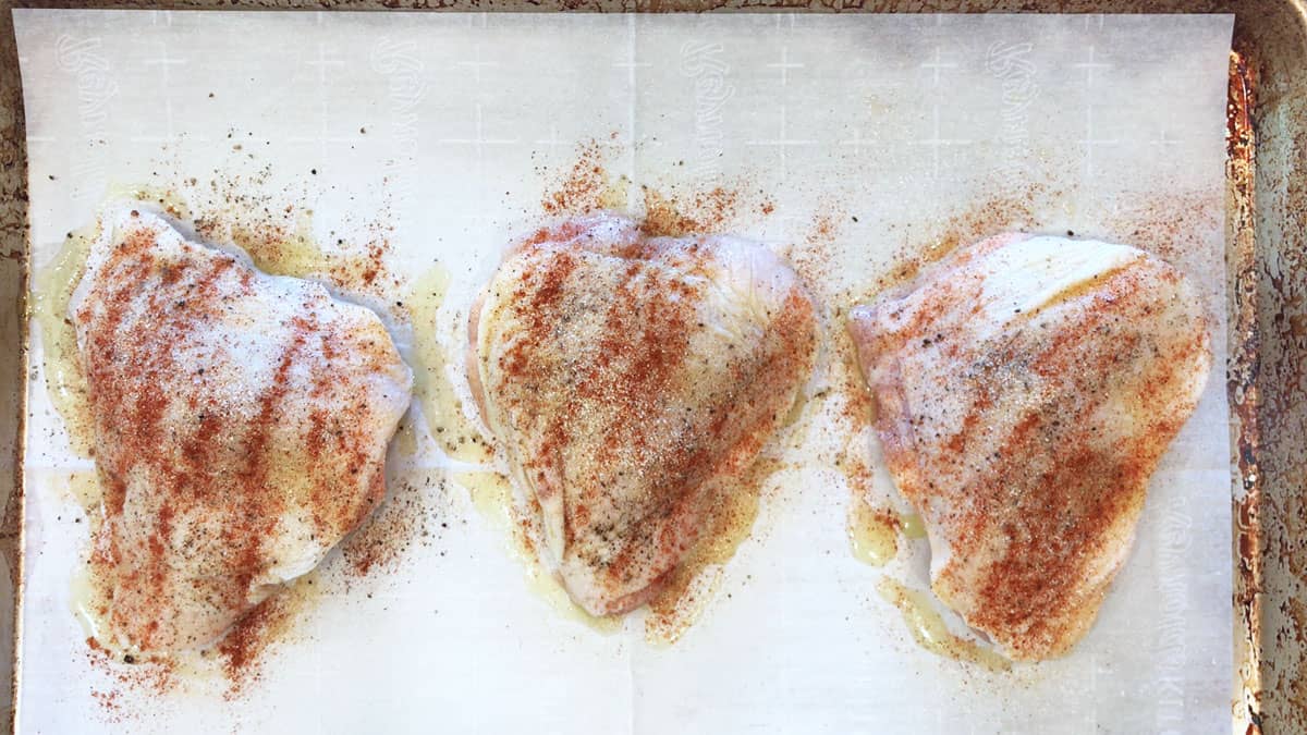Seasoned raw chicken thighs on a baking sheet.