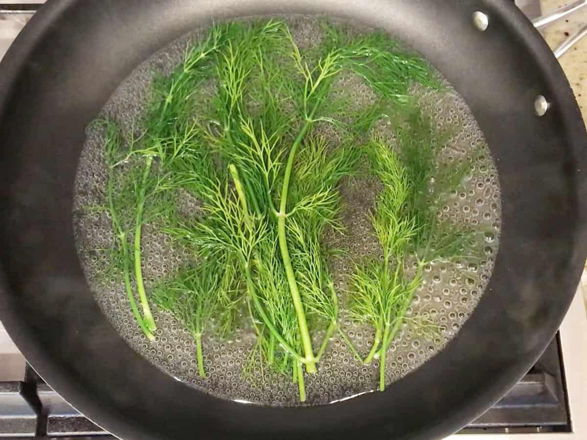 A skillet with white wine and dill sprigs.