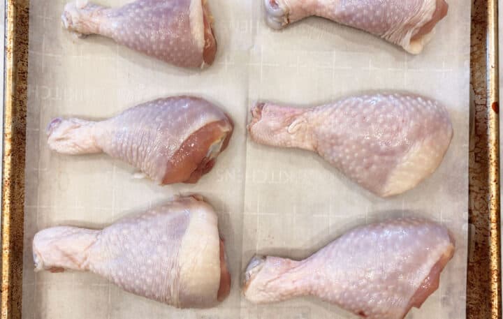 Raw drumsticks arranged on a baking sheet.