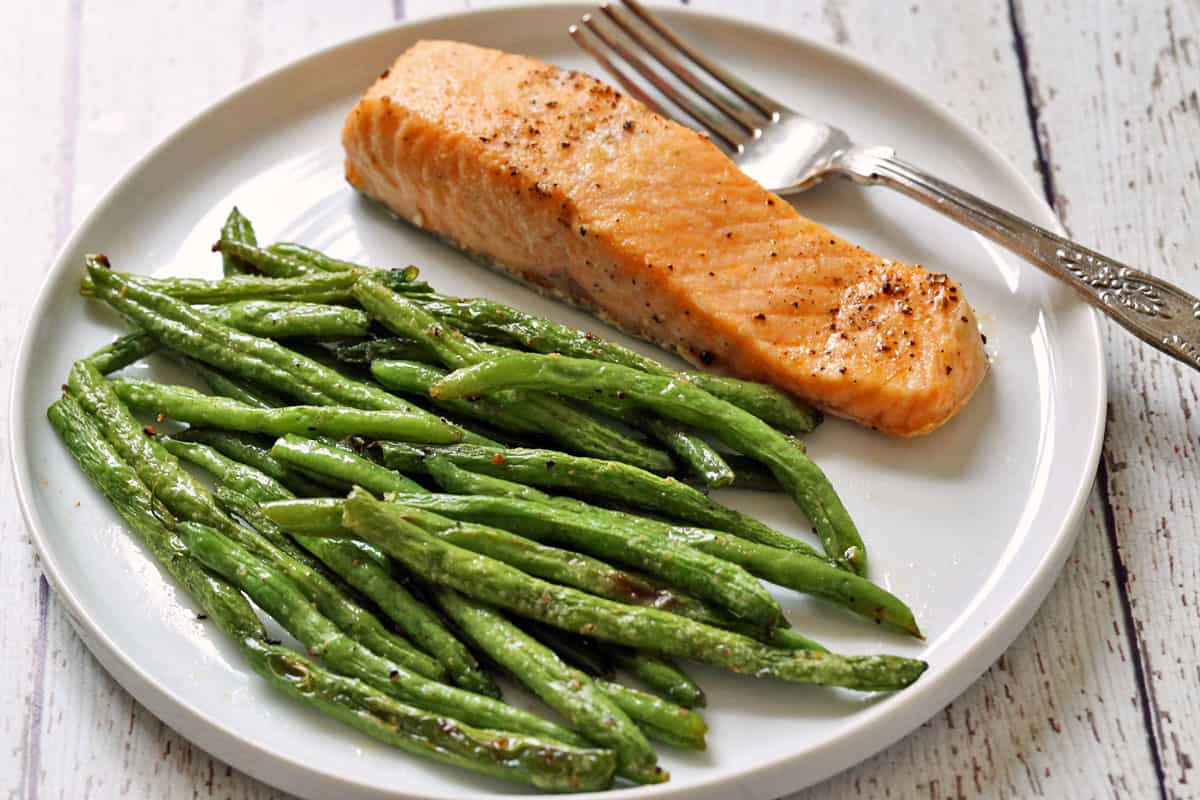 Roasted green beans and baked salmon on a white plate with a fork.