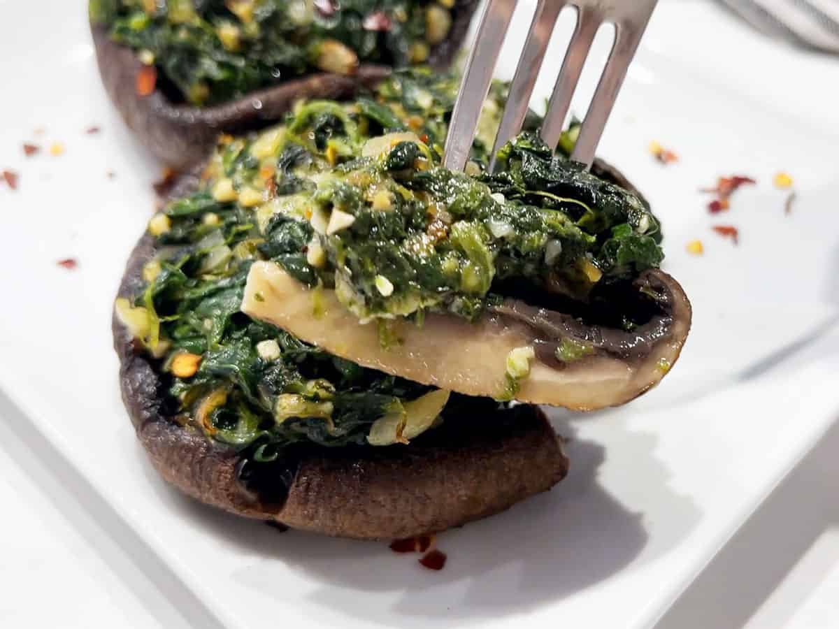 A fork holding a piece of a stuffed portobello mushroom.