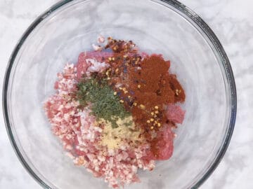 A bowl with ground beef, chopped bacon, and spices.